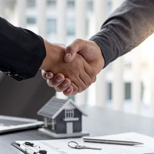 deux personnes qui se serrent la main avec un contrat posé sur un bureau