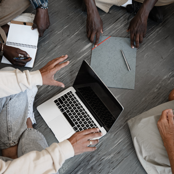 Jeunes assis en rond qui discutent avec sur le sol, un ordinateur et des stylos