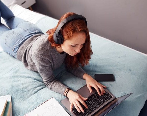 étudiante allongée sur son lit avec un casque sur les oreilles et un ordinateur